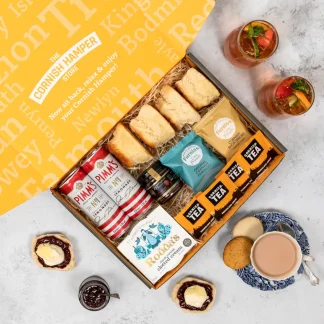 Cornish Cream Tea Hamper with Pimm's and Lemonade. The Cornish Hamper Store box is opened, showing the hamper contents on a layer of classic hamper straw. Four Cornish scones sit alongside two snack packs of Furniss biscuits, four Cornish teabags, a pot of Roddas clotted cream, a jar of strawberry jam and two cans of Pimm’s