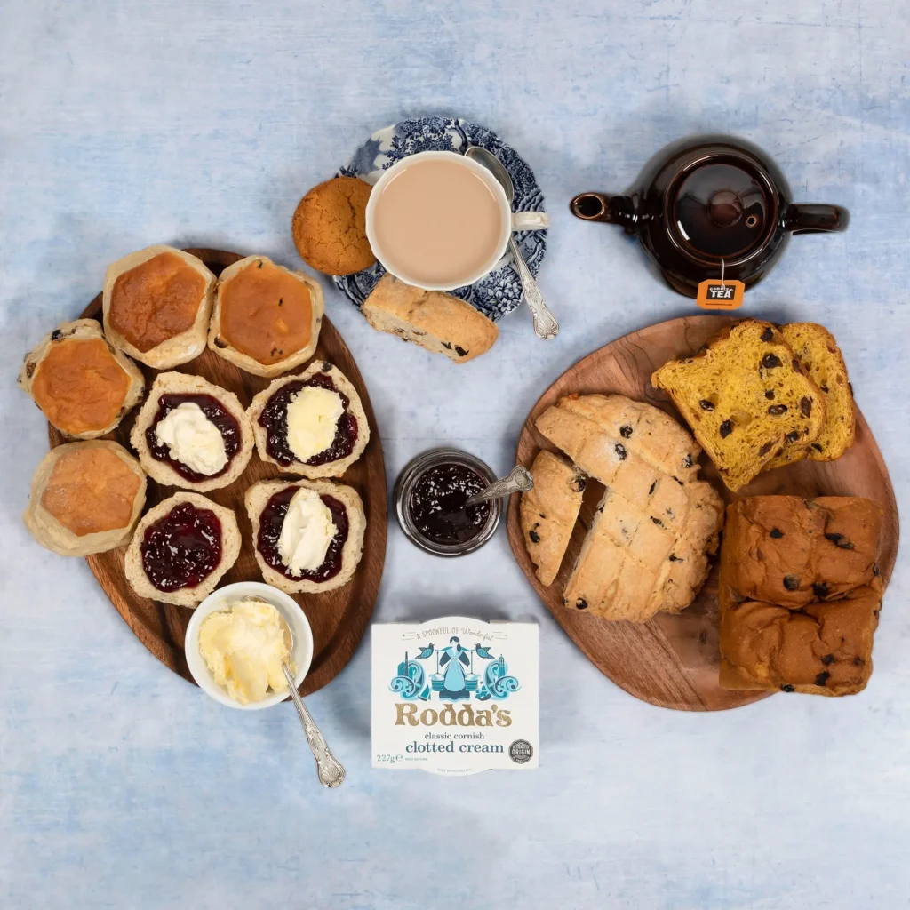 Scones topped with Jam and clotted cream can be seen on one platter, with sliced Saffron Cake and Hevva Cakes on the other