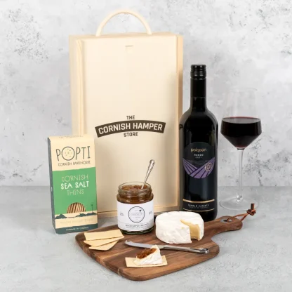 The Cheese Chutney and Wine Gift Set displayed with all hamper items in a row next to a glass of red wine. The wooden Cornish Hamper Store branded box sits in the background