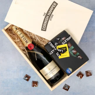 High quality Moet Champagne with gold detail presented on a bed of straw inside a branded gift box. A black box of Taste of the West winner Langleys chocolate rests beside the bottle