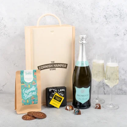 The Prosecco and Chocolate Gift displayed with all hamper items in a row next to two glasses of Prosecco and wooden gift box