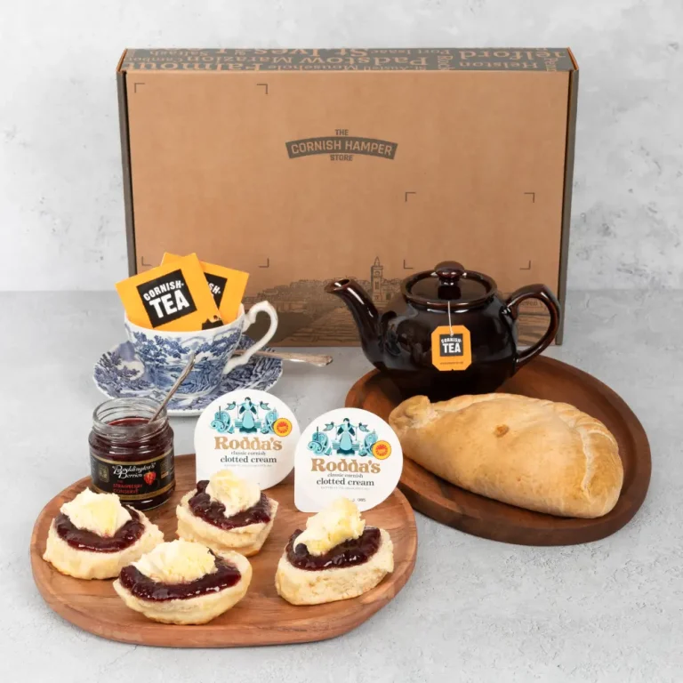 A handmade Cornish pasty sits beside a plate of Cornish cream teas. The scones are topped with jam and cream