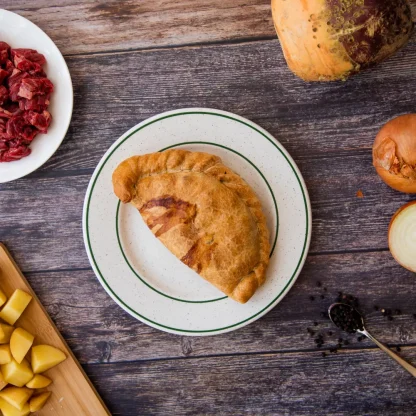 The Cornish Pasty rests on a plate surrounded by ingredients