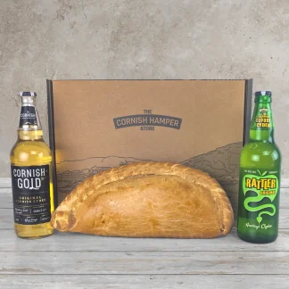 Giant Cornish Pasty surrounded by a bottle of Cornish Gold Cyder, a bottle of Rattler Original Cornish Cyder and a The Cornish Hamper Store box