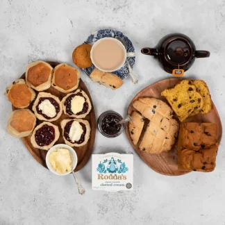 Cornish Afternoon tea served on wooden serving platters. Scones topped with Cornish Jam and Rodda's clotted cream can be seen on one platter, with sliced Saffron Cake and Hevva Cakes on the other