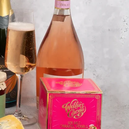 Close up image of the bright pink willies salted caramel pearls box next to a full glass of pink prosecco with the bottle of Prosecco Rosé in the background