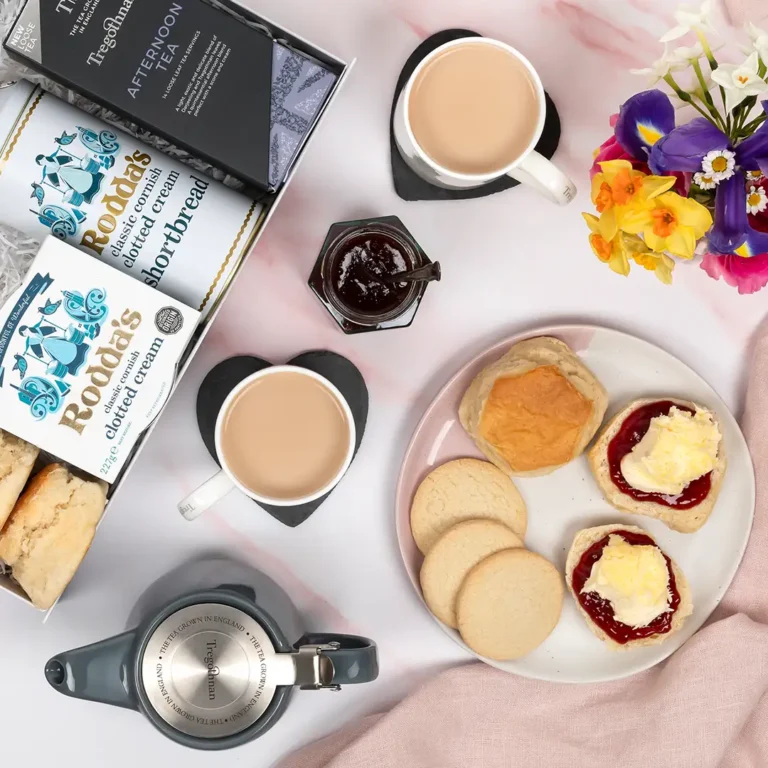 Scones topped with jam and cream next to mugs of cornish tea